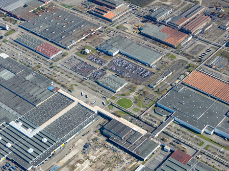 Aerial view of vast industrial complex with geometric rooftops and orderly parking lots creating a stark contrast against the central green roundabout Sausheim Grand Est France.