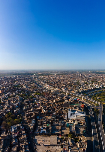 Aerial view of the dense urban landscape featuring a prominent highway bridge winding through the city rooftops under a clear blue sky in Lahore Punjab Pakistan.