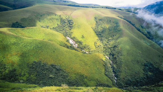 Aerial view of rolling emerald hills bathed in dappled light revealing a shimmering cascade amidst verdant valleys and misty peaks Obudu Cross River Nigeria.