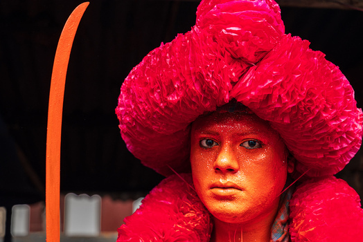 Munshiganj Bangladesh 13 April 2026 View of a person in traditional festival attire with orange face paint and a large pink ruffled headpiece holding a sword.