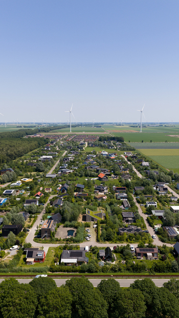 Aerial view of Ecodorp Bolderburen featuring sustainable houses with green roofs and lush gardens surrounded by open fields and wind turbines in Almere Flevoland Netherlands. Aerial view of Ecodorp Bolderburen featuring sustainable houses with green roofs and lush gardens surrounded by open fields and wind turbines in Almere Flevoland Netherlands.
