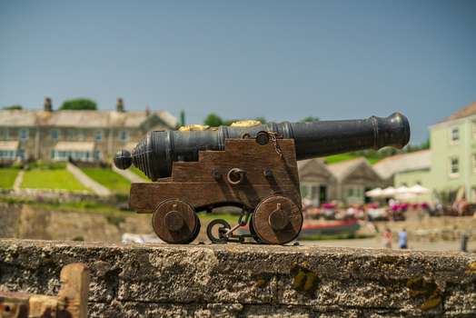 View of an antique cannon on a wooden carriage resting on a stone wall in the historic harbor village of Charlestown Cornwall United Kingdom. View of an antique cannon on a wooden carriage resting on a stone wall in the historic harbor village of Charlestown Cornwall United Kingdom.