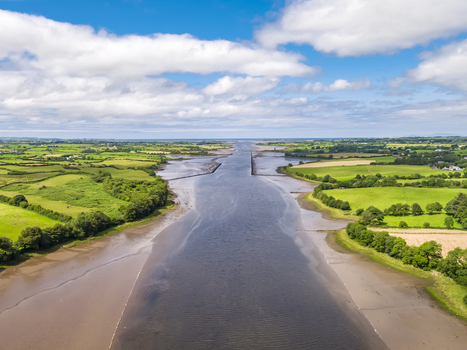 Aerial view of the River Moy estuary flowing through lush green fields and rural landscape under a blue sky with white clouds in Ballina County Mayo Ireland.