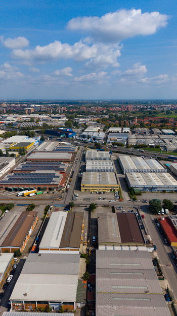 Aerial view of manufacturing and logistics buildings with rooftop solar panels surrounded by industrial infrastructure and roads in San Giuliano Milanese Lombardy Italy.