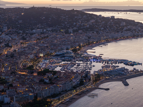 Aerial view of Cannes at dusk featuring the illuminated harbor with yachts sandy beaches and dense urban architecture in Cannes Provence Alpes Cote d Azur France. Aerial view of Cannes at dusk featuring the illuminated harbor with yachts sandy beaches and dense urban architecture in Cannes Provence Alpes Cote d Azur France.