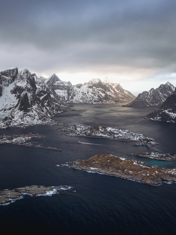 Aerial view of jagged snow dusted peaks embracing the tranquil island dotted waters below Reinebringen Nordland Norway.