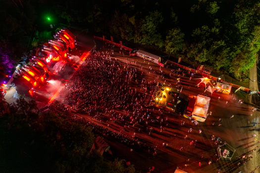 Herzogenaurach Germany 26 July 2025 Aerial view of Open Beatz Festival featuring an illuminated main stage with red lights a large crowd of people and white tents at night.