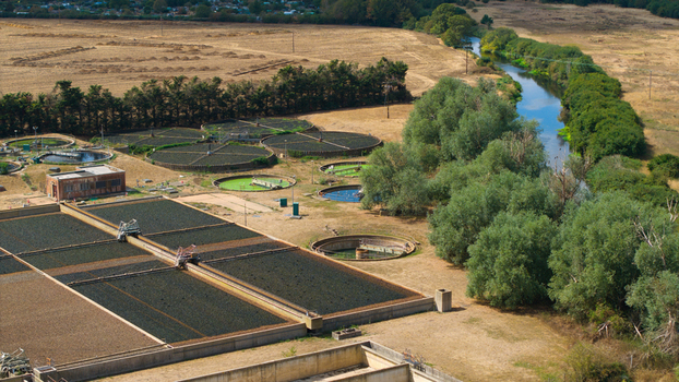 Aerial view of the wastewater treatment works featuring circular sedimentation tanks and rectangular aeration basins situated next to a river and open fields in St Neots England United Kingdom. Aerial view of the wastewater treatment works featuring circular sedimentation tanks and rectangular aeration basins situated next to a river and open fields in St Neots England United Kingdom.