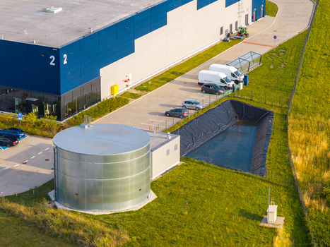 Aerial view of an industrial warehouse with a large metal water tank parking lot and retention pond in Kowale Pomeranian Voivodeship Poland. Aerial view of an industrial warehouse with a large metal water tank parking lot and retention pond in Kowale Pomeranian Voivodeship Poland.