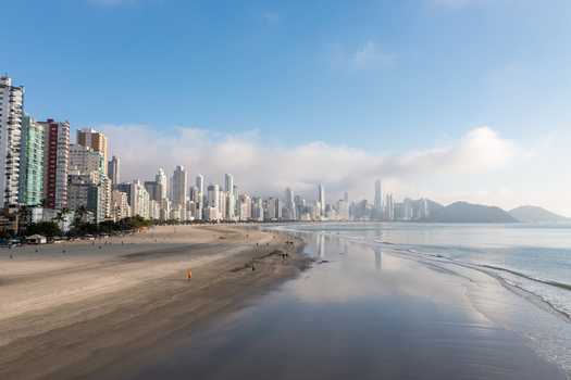 Aerial view of Balneario Camboriu skyline and sandy beach with people walking along the shore and ocean reflections Balneario Camboriu State of Santa Catarina Brazil. Aerial view of Balneario Camboriu skyline and sandy beach with people walking along the shore and ocean reflections Balneario Camboriu State of Santa Catarina Brazil.