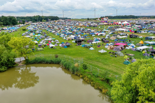 Aerial view of Open Beatz Festival camping grounds with numerous colorful tents a small pond and wind turbines under a cloudy sky Herzogenaurach Bayern Germany. Aerial view of Open Beatz Festival camping grounds with numerous colorful tents a small pond and wind turbines under a cloudy sky Herzogenaurach Bayern Germany.