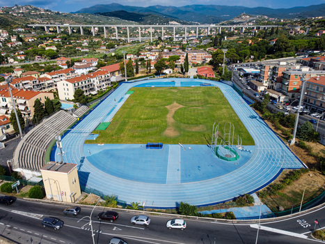 Aerial view of an athletics stadium with a blue running track and green field surrounded by residential buildings and a large viaduct in Imperia Liguria Italy. Aerial view of an athletics stadium with a blue running track and green field surrounded by residential buildings and a large viaduct in Imperia Liguria Italy.