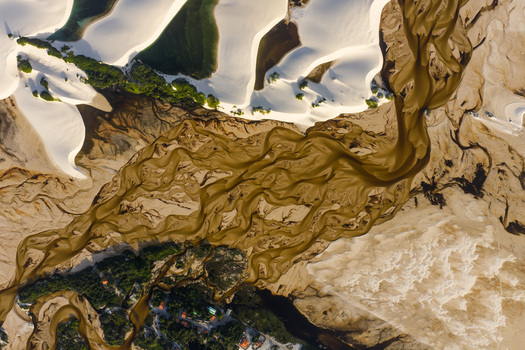 Aerial view of Parque Nacional dos Lencois Maranhenses with a winding brown river flowing through white sand dunes and green vegetation in Lencois Maranhenses MA Brazil. Aerial view of Parque Nacional dos Lencois Maranhenses with a winding brown river flowing through white sand dunes and green vegetation in Lencois Maranhenses MA Brazil.