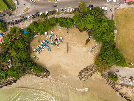 Aerial view of colorful fishing boats parked on a sandy beach surrounded by lush green trees and a coastal road with vehicles in Galle Southern Province Sri Lanka. Aerial view of colorful fishing boats parked on a sandy beach surrounded by lush green trees and a coastal road with vehicles in Galle Southern Province Sri Lanka.