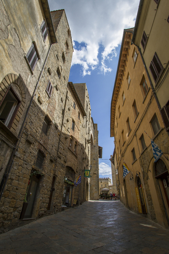 View of aged stone buildings cast long shadows on a narrow cobblestone street under a radiant blue sky Volterra Tuscany Italy. View of aged stone buildings cast long shadows on a narrow cobblestone street under a radiant blue sky Volterra Tuscany Italy.