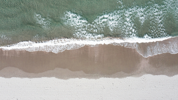 Aerial view of Omaha Beach with white sand gentle waves and clear turquoise water in Omaha Auckland New Zealand.