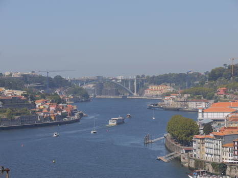 View of the Douro River with the Arrabida Bridge in the background surrounded by historic buildings and lush trees along the riverbanks in Porto Porto District Portugal. View of the Douro River with the Arrabida Bridge in the background surrounded by historic buildings and lush trees along the riverbanks in Porto Porto District Portugal.