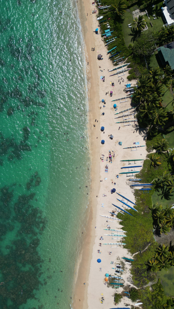 Aerial view of the white sands of Lanikai Beach meeting the turquoise water lined with vibrant green trees and colorful boats Kailua Hawaii United States. Aerial view of the white sands of Lanikai Beach meeting the turquoise water lined with vibrant green trees and colorful boats Kailua Hawaii United States.