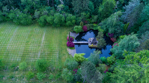 Aerial view of a serene garden pond with a wooden gazebo and bridge surrounded by lush trees and a mown lawn in Portland Oregon United States. Aerial view of a serene garden pond with a wooden gazebo and bridge surrounded by lush trees and a mown lawn in Portland Oregon United States.