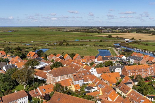 View of the historic red tiled rooftops and winding river of the old town surrounded by flat green marshlands under a blue sky in Ribe Denmark. View of the historic red tiled rooftops and winding river of the old town surrounded by flat green marshlands under a blue sky in Ribe Denmark.