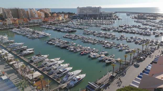 Aerial view of Vilamoura Marina filled with numerous yachts and boats docked along the piers surrounded by modern buildings and palm trees in Quarteira Faro District Portugal.