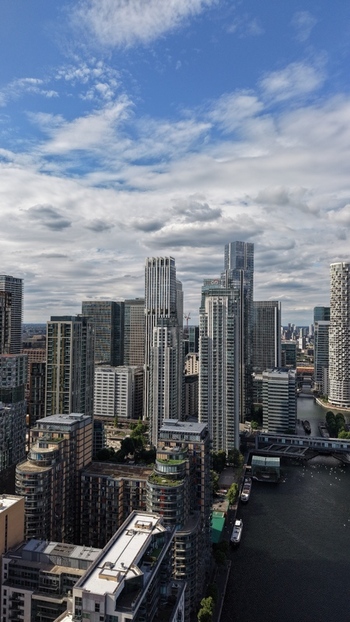London United Kingdom 16 June 2026 Aerial view of the modern skyscrapers of Canary Wharf district with the River Thames and a cloudy blue sky.