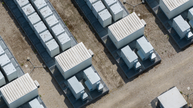 Aerial view of a battery energy storage system with rows of white industrial containers arranged on metal platforms over a gravel site in Wanneperveen Overijssel Netherlands.