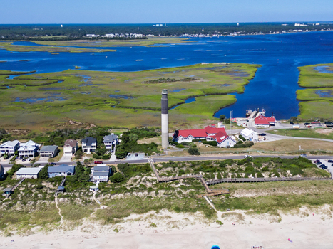 Aerial view of Oak Island Lighthouse surrounded by coastal salt marshes sandy beaches and residential houses in Caswell Beach North Carolina United States.
