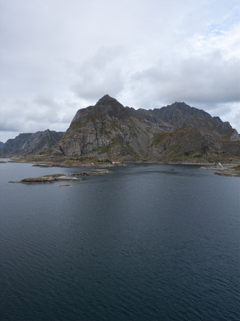 Aerial view of Rorvikstranda beach and the rugged rocky mountains rising from the dark sea under an overcast sky in Henningsvaer Nordland Norway.