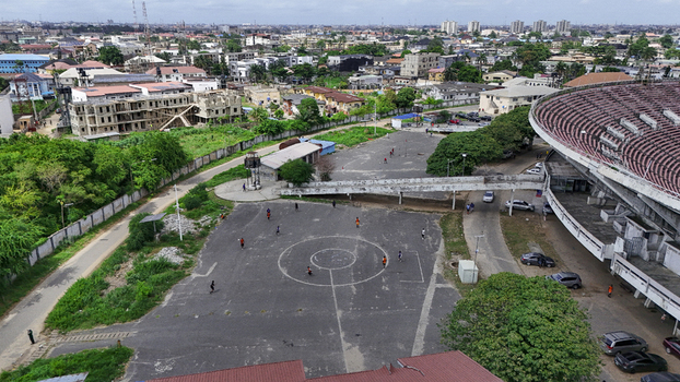 Aerial view of National Stadium Surulere Lagos with people playing on an outdoor court surrounded by urban buildings and lush greenery Lagos Lagos Nigeria. Aerial view of National Stadium Surulere Lagos with people playing on an outdoor court surrounded by urban buildings and lush greenery Lagos Lagos Nigeria.