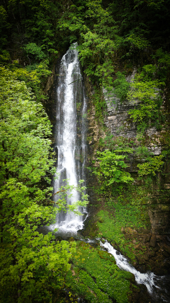 Aerial view of Cascades du Flumen waterfall cascading down a rocky cliff surrounded by dense green forest in Septmoncel Les Molunes Bourgogne Franche Comte France. Aerial view of Cascades du Flumen waterfall cascading down a rocky cliff surrounded by dense green forest in Septmoncel Les Molunes Bourgogne Franche Comte France.