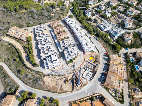 Aerial view of modern residential villas with flat roofs swimming pools and ongoing construction work with a crane in Moraira Valencian Community Spain.