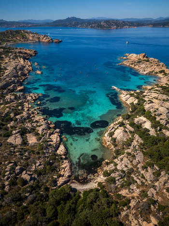 Aerial view of the turquoise water of a secluded bay surrounded by granite rocks and Mediterranean scrub in La Maddalena Sardinia Italy. Aerial view of the turquoise water of a secluded bay surrounded by granite rocks and Mediterranean scrub in La Maddalena Sardinia Italy.