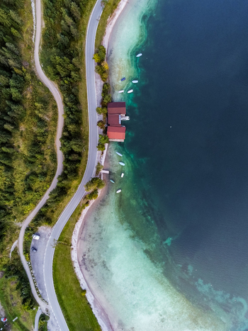 Aerial view of Plansee lake with a boathouse small boats moored along the shore and a winding road through the forest in Reutte District Tyrol Austria. Aerial view of Plansee lake with a boathouse small boats moored along the shore and a winding road through the forest in Reutte District Tyrol Austria.