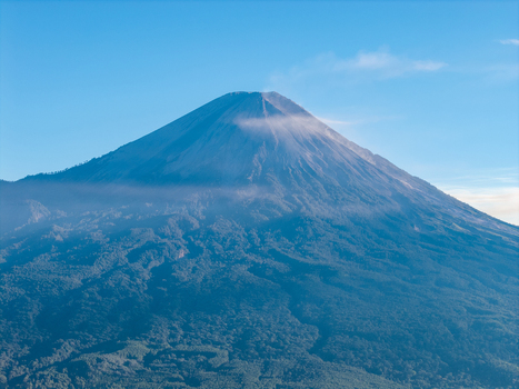 Aerial view of Mount Semeru peak rising above dense tropical forests under a clear blue sky in Kecamatan Pronojiwo Jawa Timur Indonesia.