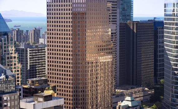 Aerial view of modern skyscrapers with glass facades reflecting sunlight overlooking the ocean and distant mountains in Vancouver British Columbia Canada.
