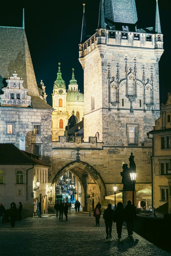Prague Prague Czechia 03 November 2021 View of the historic Charles Bridge Tower illuminated at night with gothic architecture stone archways and pedestrians on cobblestone. Prague Prague Czechia 03 November 2021 View of the historic Charles Bridge Tower illuminated at night with gothic architecture stone archways and pedestrians on cobblestone.