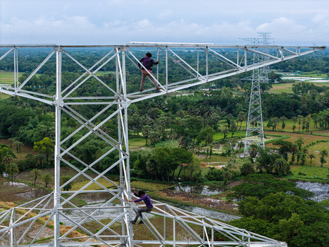 Trishal Upazila Bangladesh 13 May 2026 Aerial view of workers climbing a high voltage electricity pylon overlooking the lush green rural landscape and agricultural fields. Trishal Upazila Bangladesh 13 May 2026 Aerial view of workers climbing a high voltage electricity pylon overlooking the lush green rural landscape and agricultural fields.
