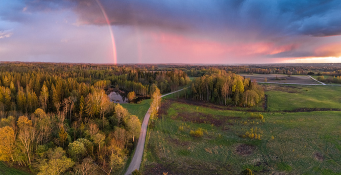 Aerial view of a rainbow over a lush forest a small pond and rural fields in Latvia. Aerial view of a rainbow over a lush forest a small pond and rural fields in Latvia.