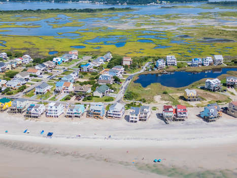 Aerial view of colorful beach houses lining the sandy shore with marshlands and tidal pools in the background in North Topsail Beach North Carolina United States.