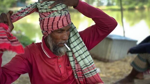 View of a man tying a turban while smoking a cigarette in Bangladesh. View of a man tying a turban while smoking a cigarette in Bangladesh.