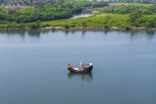 Cox s Bazar Bangladesh 11 March 2026 Aerial view of a traditional wooden fishing boat floating on the calm blue waters of a river near lush green mangroves. Cox s Bazar Bangladesh 11 March 2026 Aerial view of a traditional wooden fishing boat floating on the calm blue waters of a river near lush green mangroves.