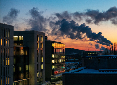 View of modern office buildings with illuminated windows at dusk set against a vibrant sunset sky with smoke rising in the distance in Vilnius Vilnius County Lithuania. View of modern office buildings with illuminated windows at dusk set against a vibrant sunset sky with smoke rising in the distance in Vilnius Vilnius County Lithuania.