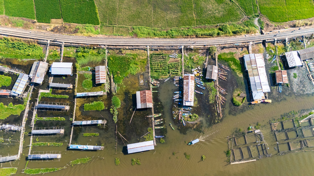 Aerial view of Lake Rawa Pening featuring traditional stilt houses fish farms and a railway track running along the shore in Waduk Rawapening Central Java Indonesia. Aerial view of Lake Rawa Pening featuring traditional stilt houses fish farms and a railway track running along the shore in Waduk Rawapening Central Java Indonesia.