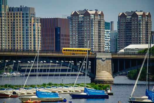 Boston United States 13 June 2025 View of Charles River with sailboats moored in the foreground and a yellow school bus crossing the bridge against a backdrop of city skyscrapers. Boston United States 13 June 2025 View of Charles River with sailboats moored in the foreground and a yellow school bus crossing the bridge against a backdrop of city skyscrapers.