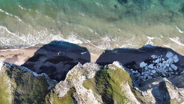Aerial view of Bulbjerg cliff featuring dramatic limestone formations rocky debris on the sandy beach and turquoise sea waves crashing against the shore in Thisted Municipality Denmark. Aerial view of Bulbjerg cliff featuring dramatic limestone formations rocky debris on the sandy beach and turquoise sea waves crashing against the shore in Thisted Municipality Denmark.