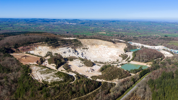 Aerial view of a vast quarry carved into the earth contrasting sharply with the surrounding verdant forests and distant town &Eacute;chassi&egrave;res Auvergne Rh&ocirc;ne Alpes France.