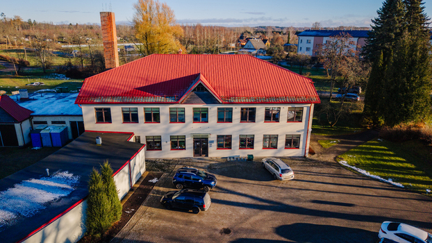 Burtnieki Latvia 22 November 2025 Aerial view of a rural school building with a distinctive red roof surrounded by trees and a parking area on a sunny late autumn day.