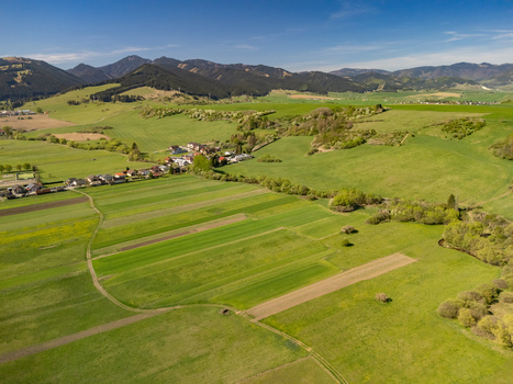 Aerial view of lush green agricultural fields and the village of Partizanska Lupca with forested mountains under a clear sky Partizanska Lupca Zilina Region Slovakia.