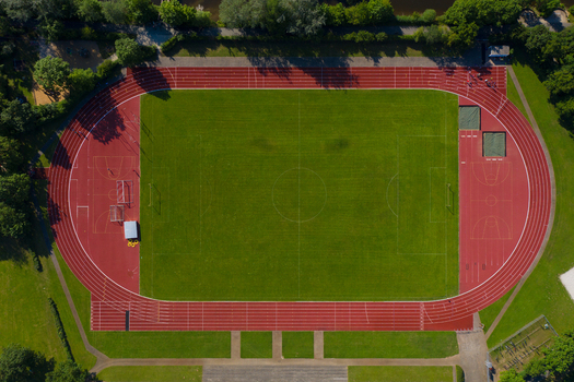 Aerial view of the Sport Island Forchheim featuring a green football pitch red running track and basketball courts surrounded by lush trees in Forchheim Bavaria Germany. Aerial view of the Sport Island Forchheim featuring a green football pitch red running track and basketball courts surrounded by lush trees in Forchheim Bavaria Germany.